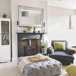 grey living room with a wall-mounted mirror above a fire place topped with candles and floral accessories and a grey chair sofa with a green pillow and grey furniture