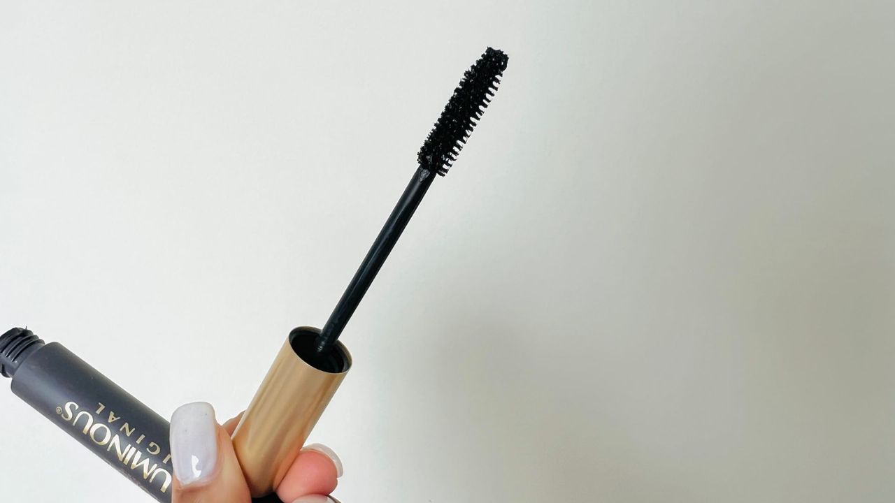 A person holding an opened L'Oreal Voluminous Original mascara tube, showing the mascara's wand and brush for the best L'Oreal mascara.
