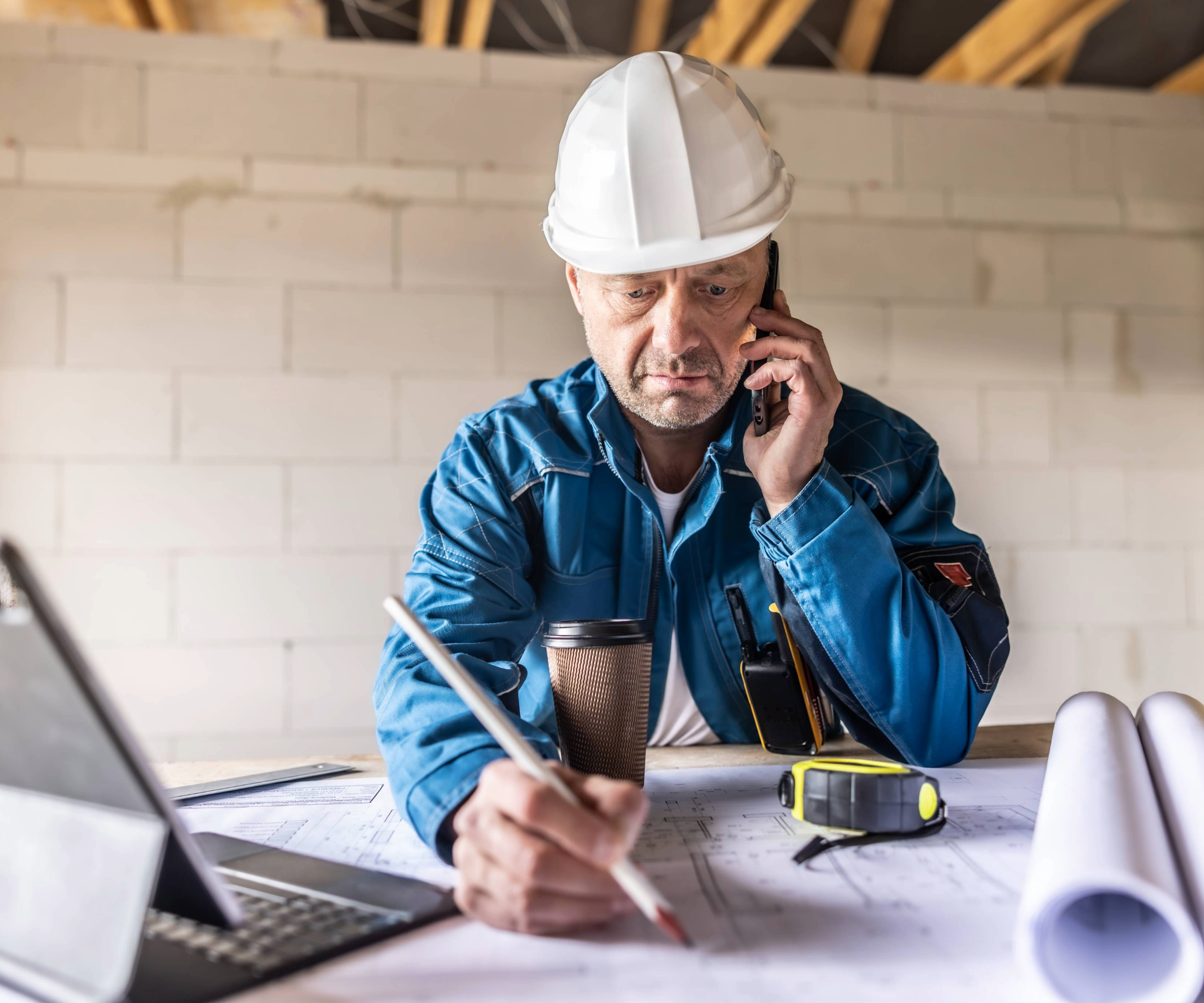 Man sitting at a desk on the phone with a builder&#039;s hat on