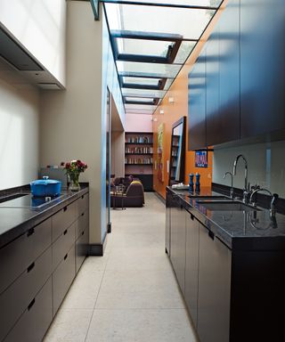 A black galley kitchen idea in a narrow room with orange wall and skylights.