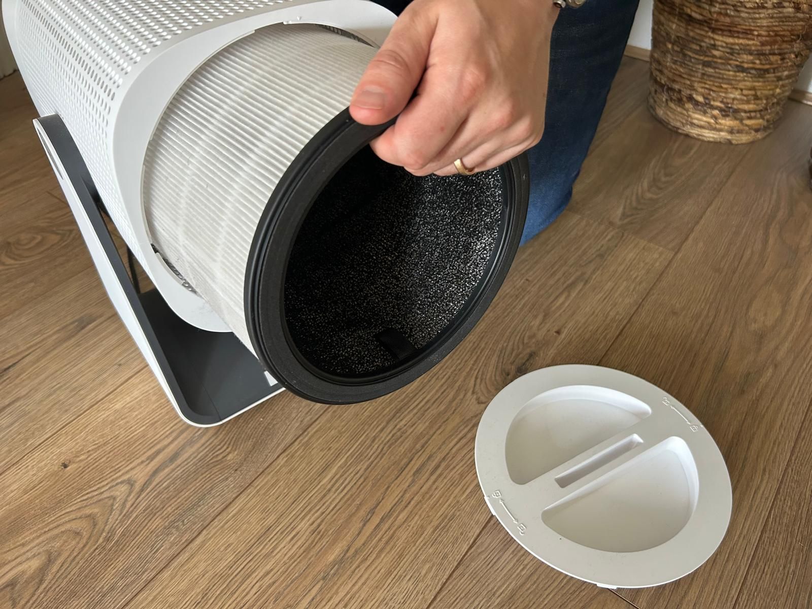 Removing the filter from the Coway Airmega Aim, with hand pulling filter out of the air purifier on wooden floor, during testing in Gabriella's home