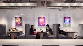 People using laptops and smiling in front of bright neon art