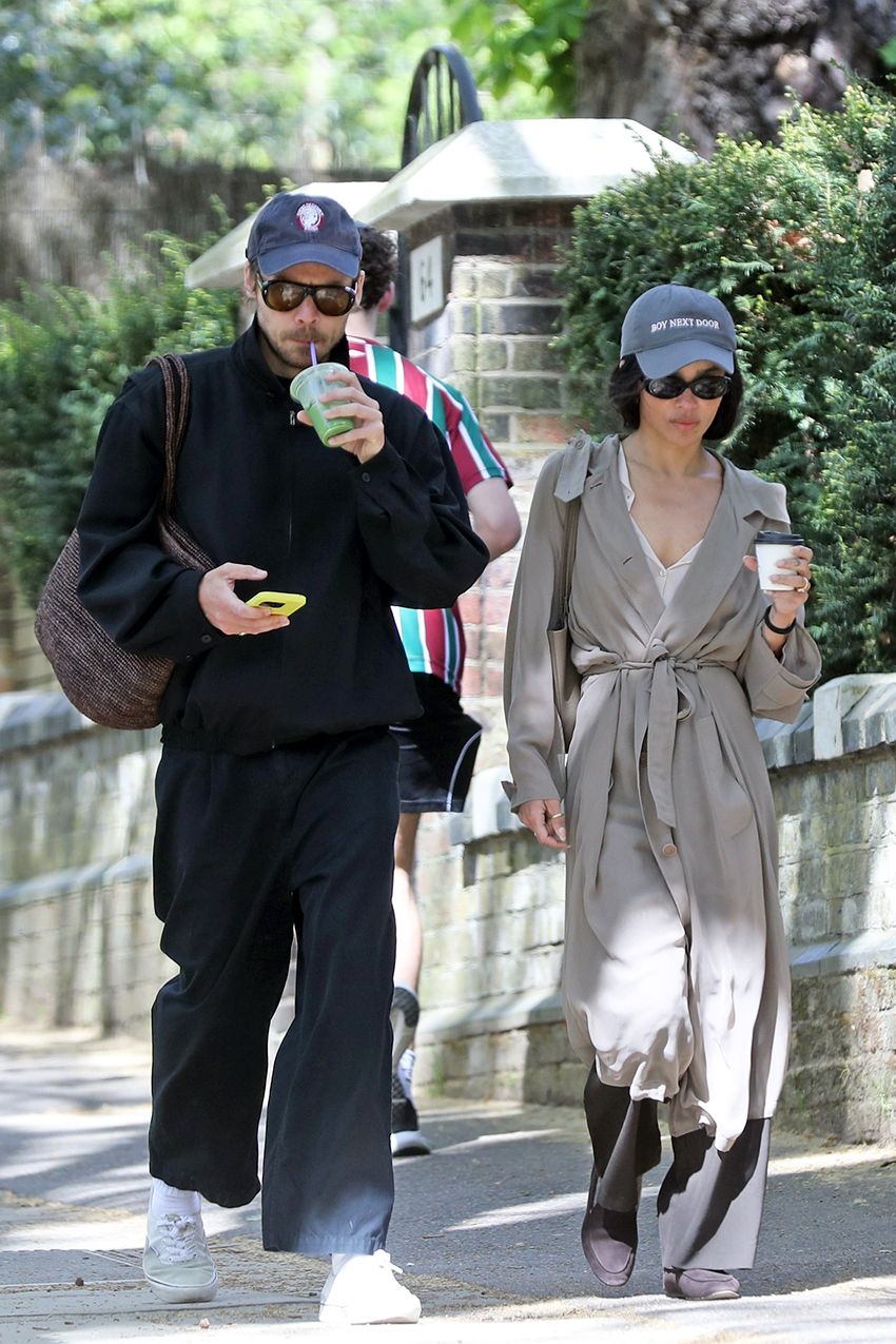 Zoe Kravitz wearing a navy baseball cap, tan trench coat, white blouse, black pants, and The Row soft loafers