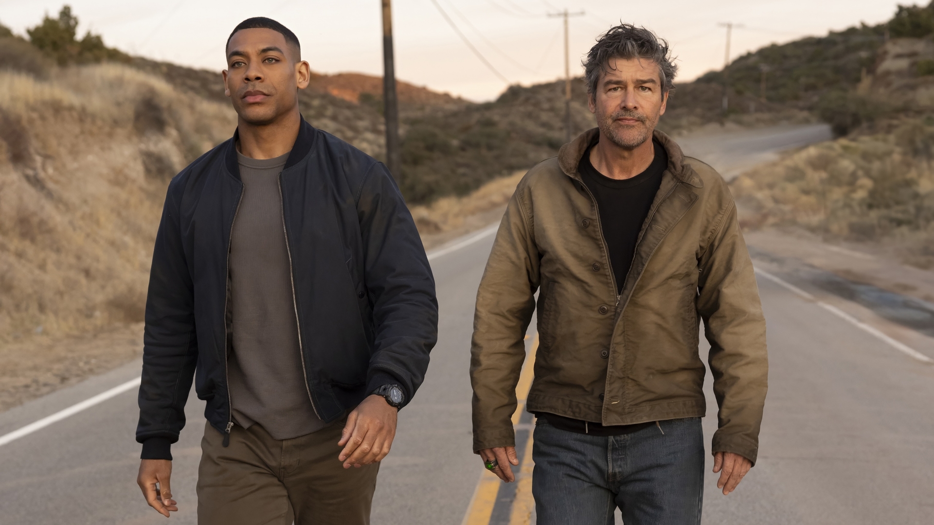 Aaron Pierre as John Stewart and Kyle Chandler as Hal Jordan walking on a road.
