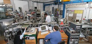Image shows scientists gathered around the Helium Spin-Echo apparatus in the lab