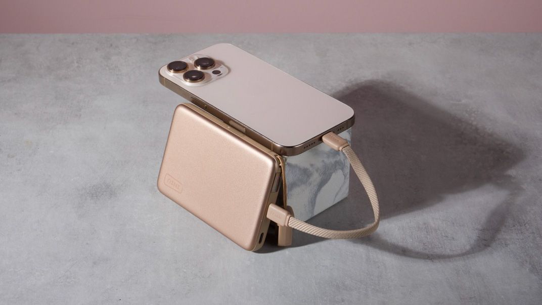 An Iniu SnapGo Air 10000mAh Power Bank leant against a marble block with an iPhone 16 Pro resting on top of it — a cable connects the two.