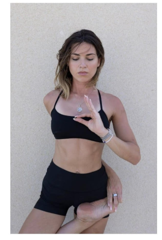 woman facing the camera wearing black crop top and shorts balancing on one leg and looking down.
