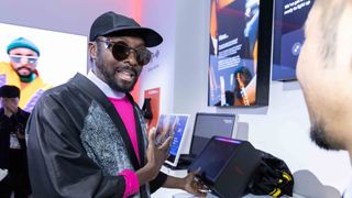 Will.i.am speaking about XBoom speakers at CES 2025, wearing all black with a black cap