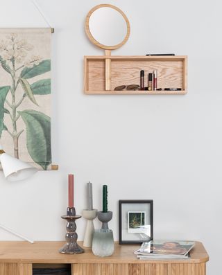 Wooden sideboard with candles in candleholders and magazines on top of it in front of white wall