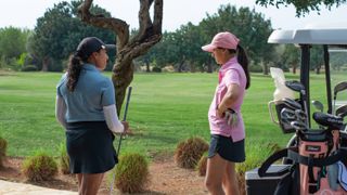 Two female golfers chatting by a golf cart