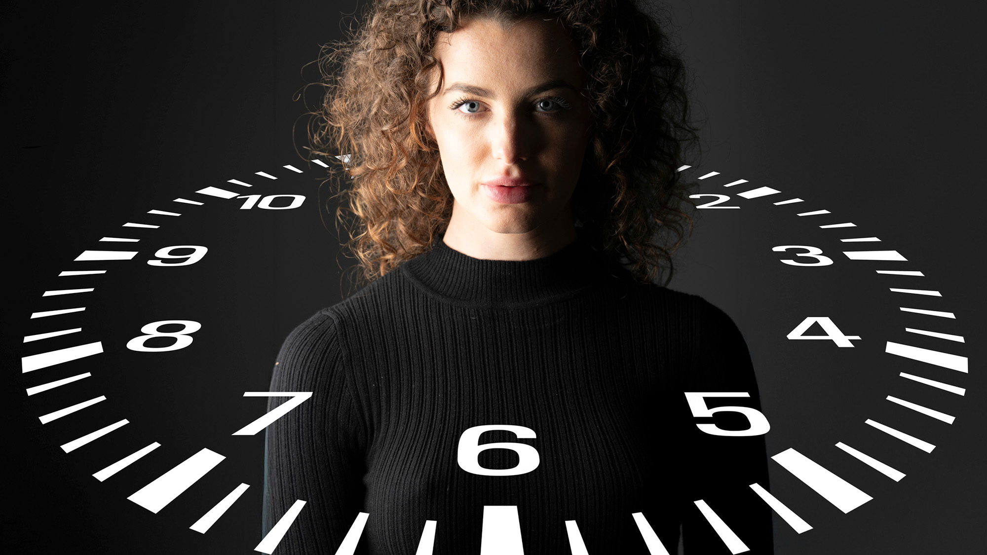 Side-lit studio portrait of model against a black background by James Paterson with a clock-face graphic