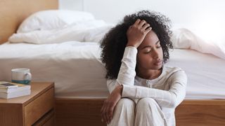 woman looking tired sitting next to a bed