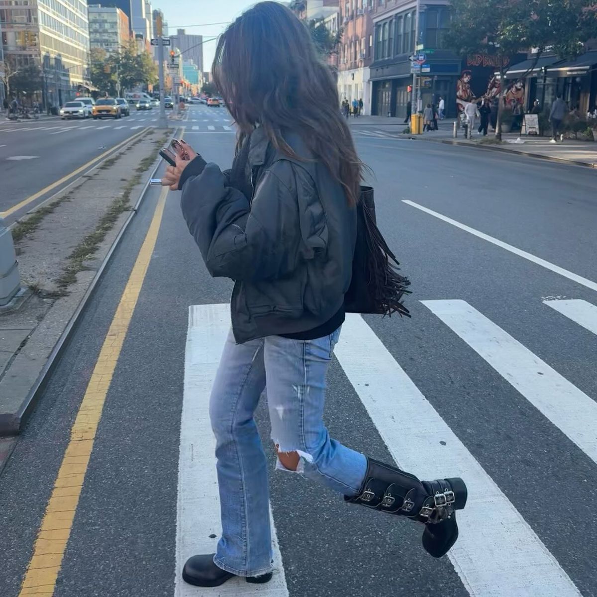 A woman crosses the street wearing skinny jeans with moto boots