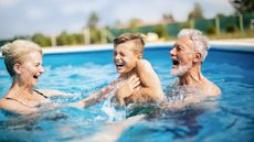 Grandparents play with their grandson in a pool.