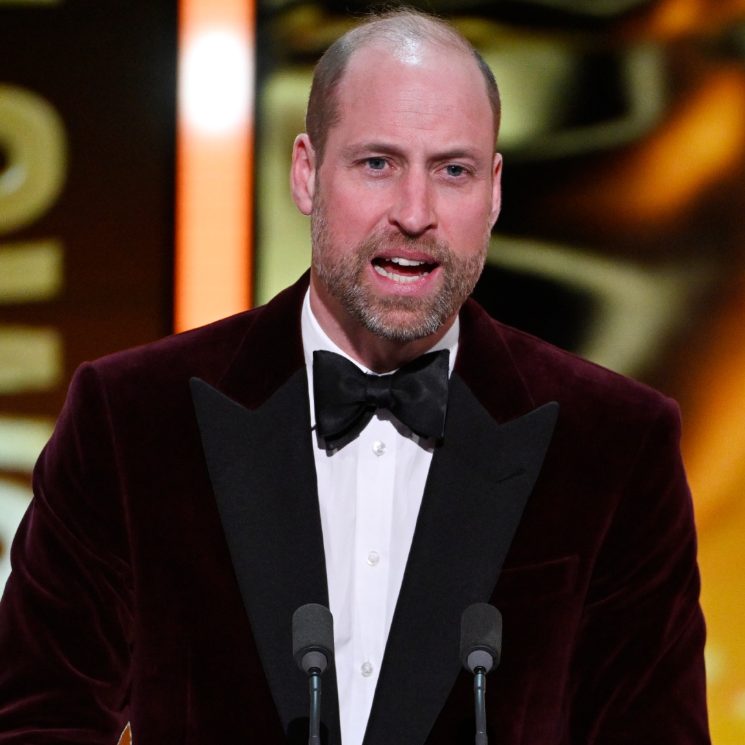 Prince William wearing a burgundy jacket and tie speaking in a mic
