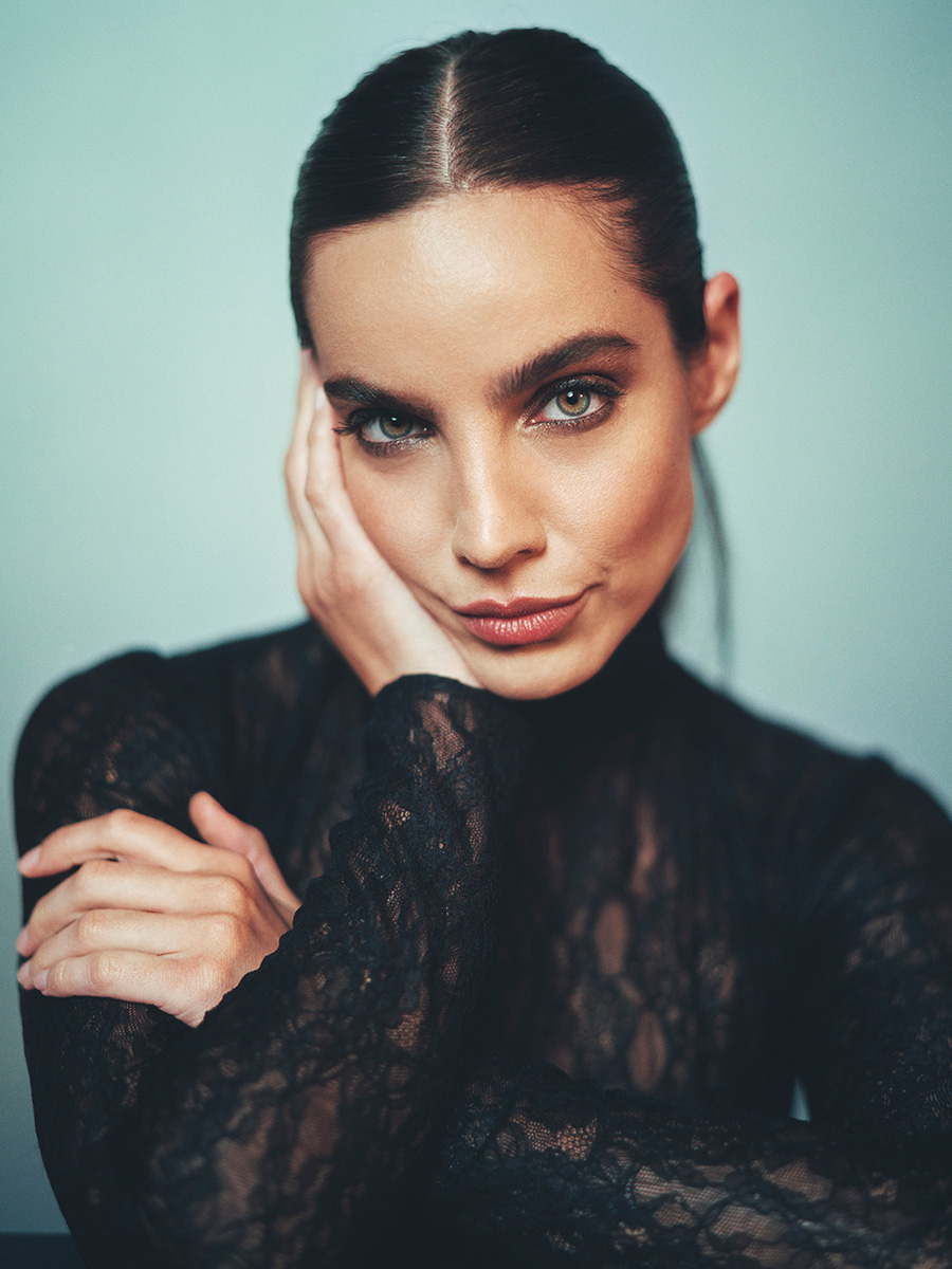 Actress María Gabriela de Faría standing in front of a light blue background and wearing a black lace long sleeve top.