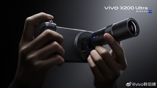 A person holds a Vivo X200 Ultra smartphone, featuring an attached 200mm Zeiss zoom lens, against a dark background