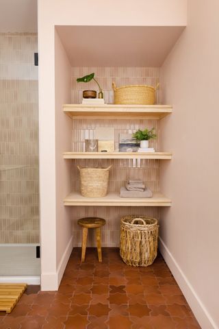 Open shelving in basement bathroom with light pink neutral wall tiling and warm terracotta floor designs