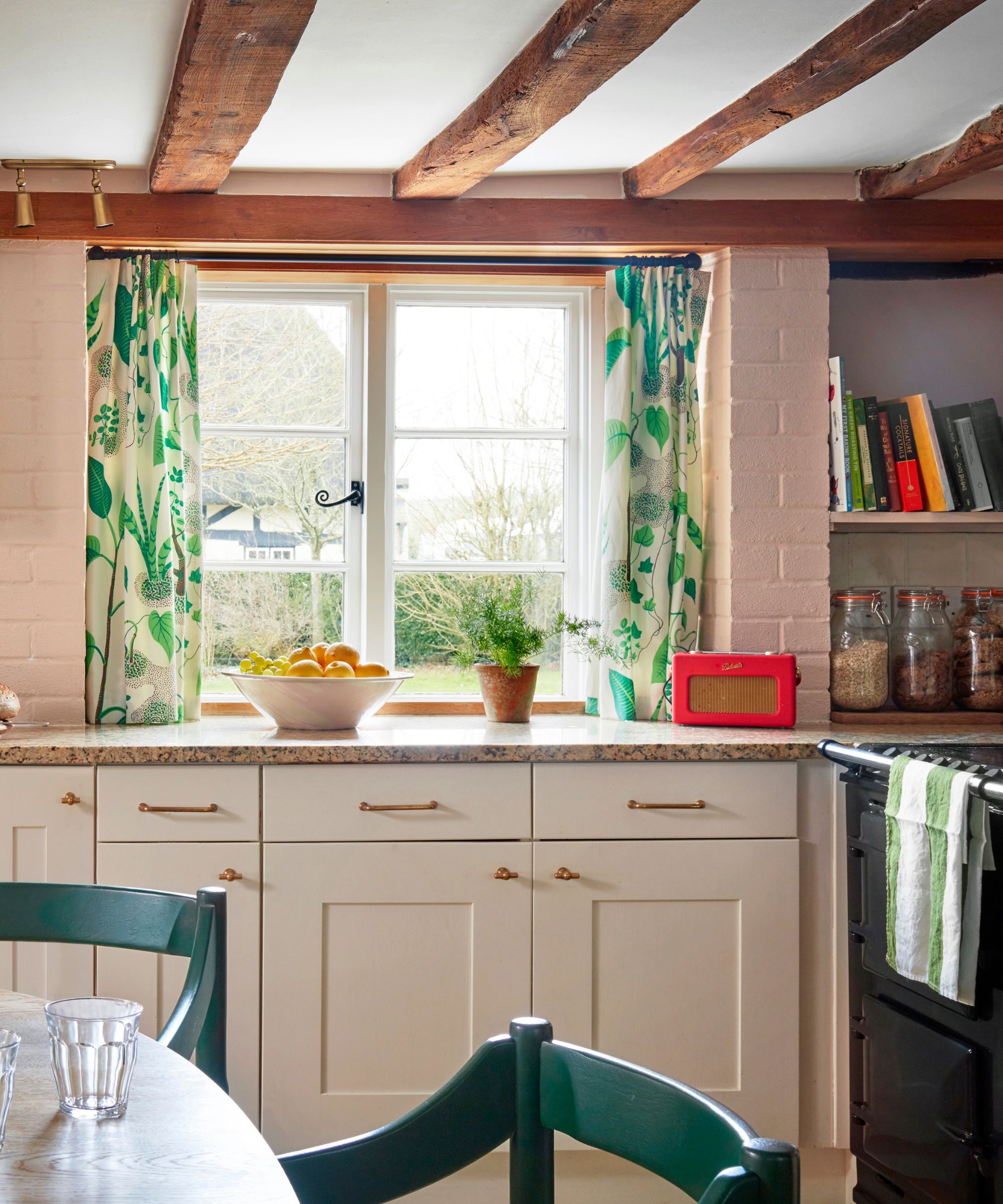 A cozy cottage kitchen with pink walls, white cabinets, and white and green curtains