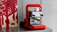 a stainless steel coffee maker wrapped in a red pip frame as modern art