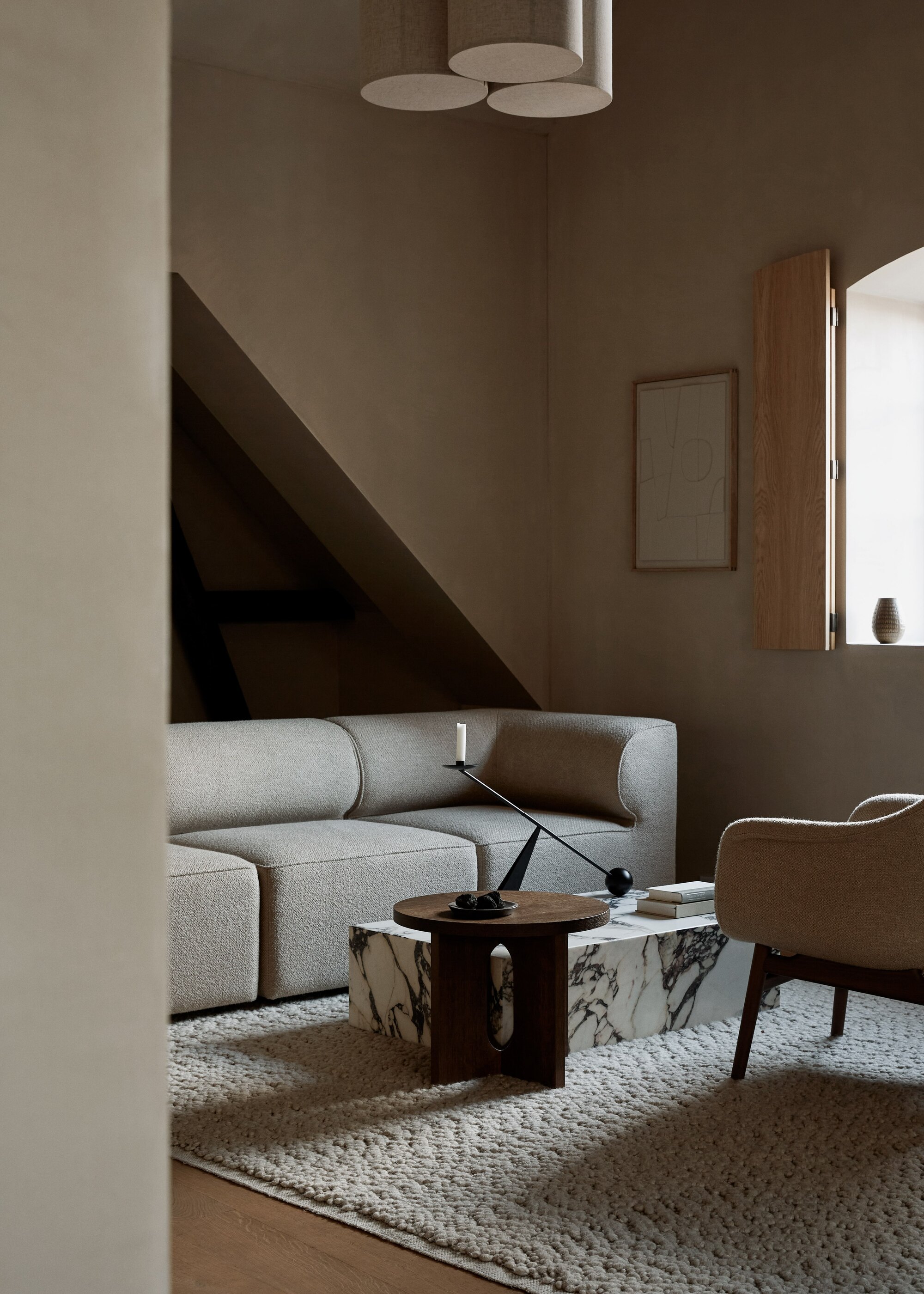 modern neutral living room with beige sofa, marble coffee table, timber side table with candlestick, beige textured rug, and beige armchair