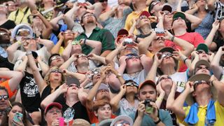 people in close proximity look up at the sky with solar glasses.