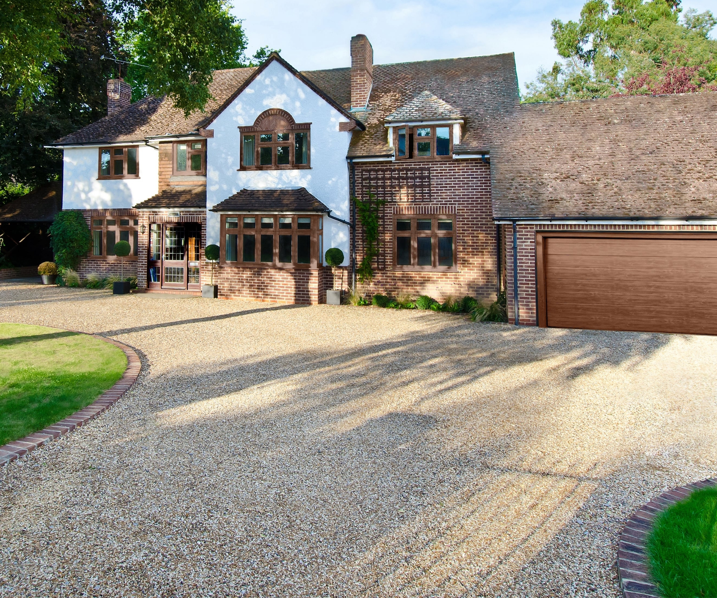 Large white and brick house with wooden-framed windows, a brick-edged gravel driveway, and double garage.