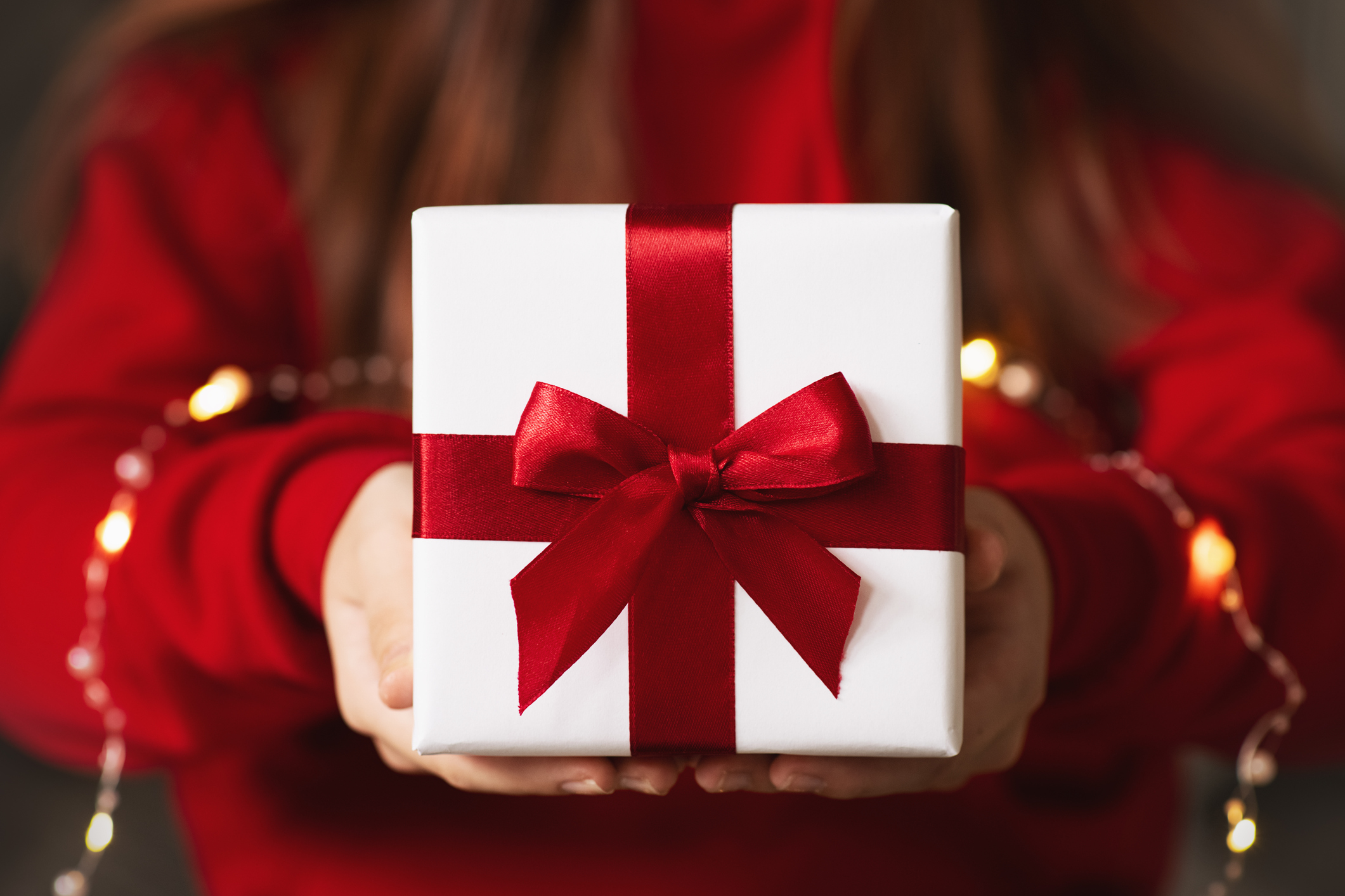 A person holding a white gift with a red ribbon.
