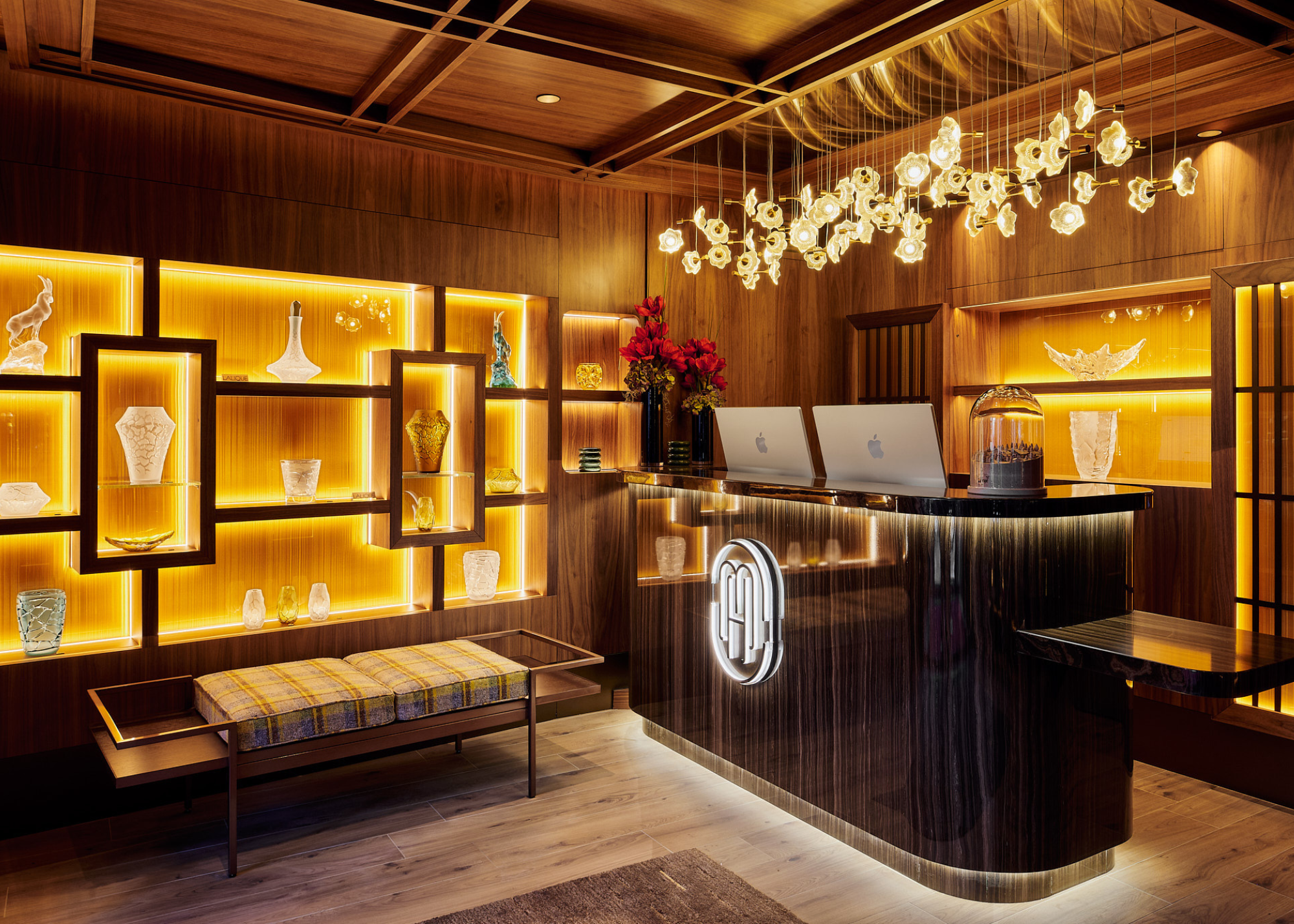 Maya Hotel Courchevel 1850 lobby with backlit alcove shelving displaying lalique crystal pieces, with a lalique lighting arrangement hanging above the reception desk