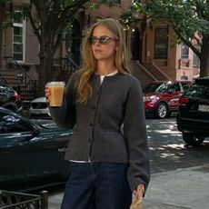 Woman wears waisted cardigan, blue jeans and black bag 