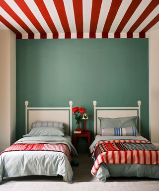 Twin bedroom with blue painted feature wall, white painted bed headboards on wall, red and white striped ceiling, two single beds with red and blue bedding