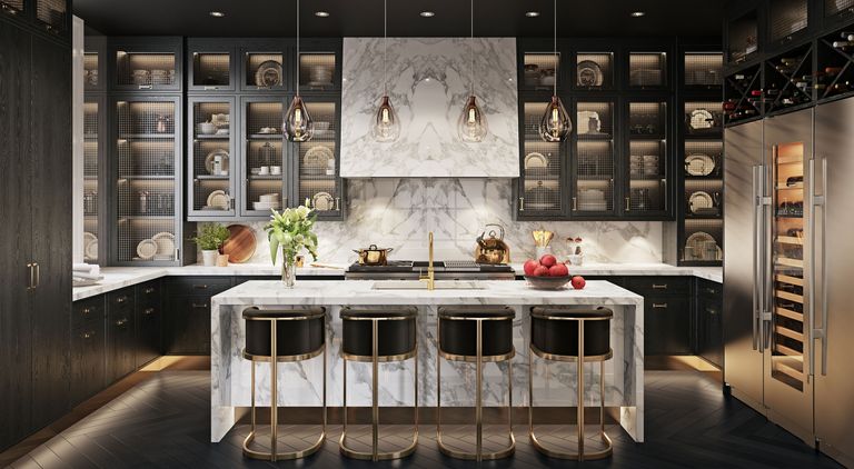 An example of kitchen island seating ideas showing a large marble island with four black and gold bar stools in front of a kitchen area with a marble backsplash and black glass-fronted cabinets