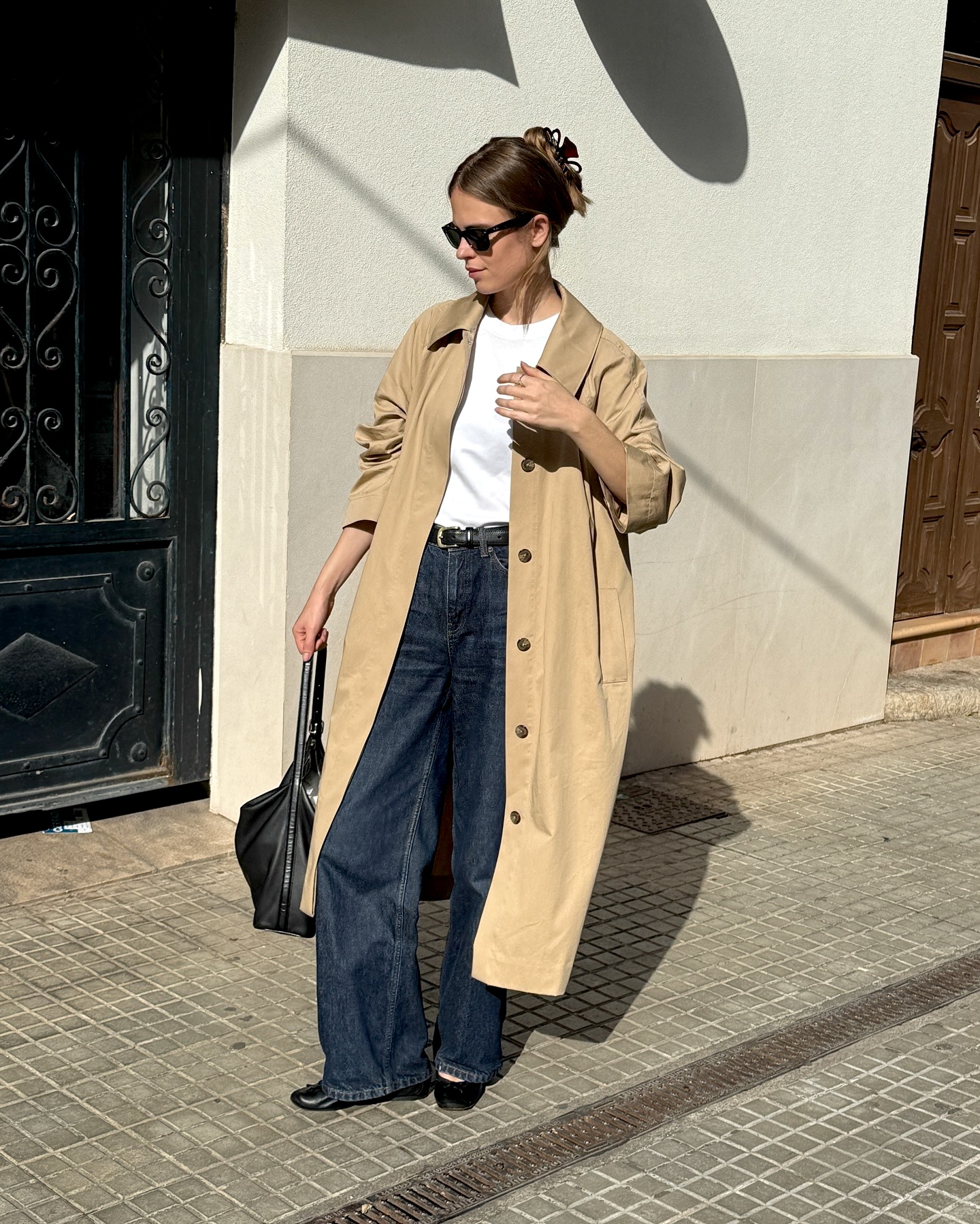 European style influencer Clara Dyrhauge wearing a fall 2025 outfit with a claw hair clip, mac trench coat, white t-shirt, black belt, dark-wash jeans, and black ballet flats