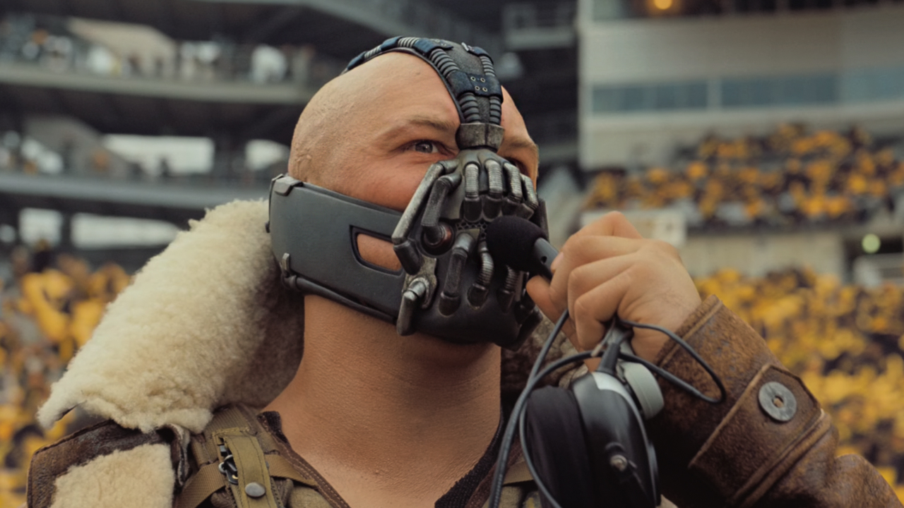 At a football game, Bane (Tom Hardy) addressed the crowd through a microphone, bundled up in a winter coat and mask. 