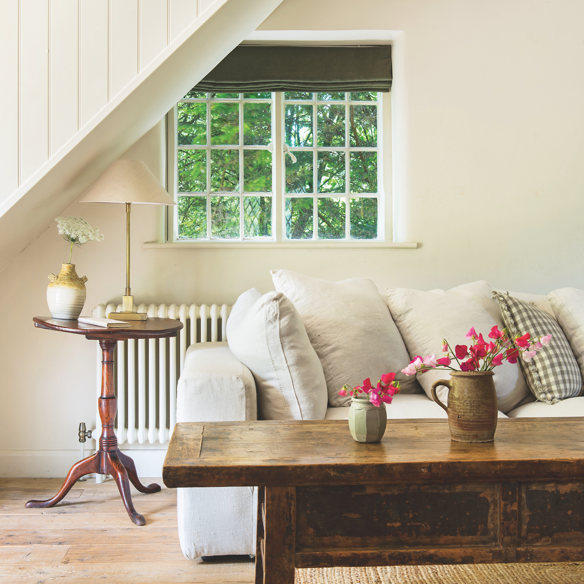 white sofa with wooden coffee table in front and small antique side table with window and white walls in living room