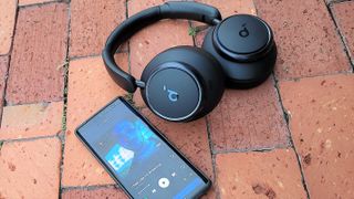 Listing image for cheap noise-cancelling headphones showing Anker Soundcore Space Q45 on brick paving with smart phone placed alongside