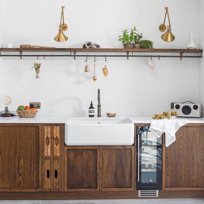 kitchen sink area with wooden storage units, underneath wooden shelf and gold light fittings