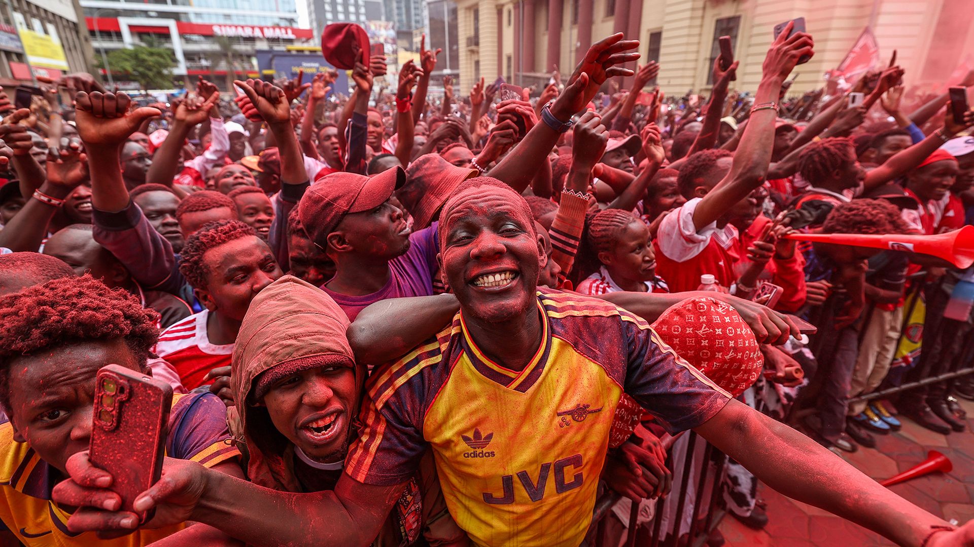 
                                Football fans coated in red powder celebrate Arsenal FC's first Premier League title win in 22 years, in Nairobi, Kenya
                            
