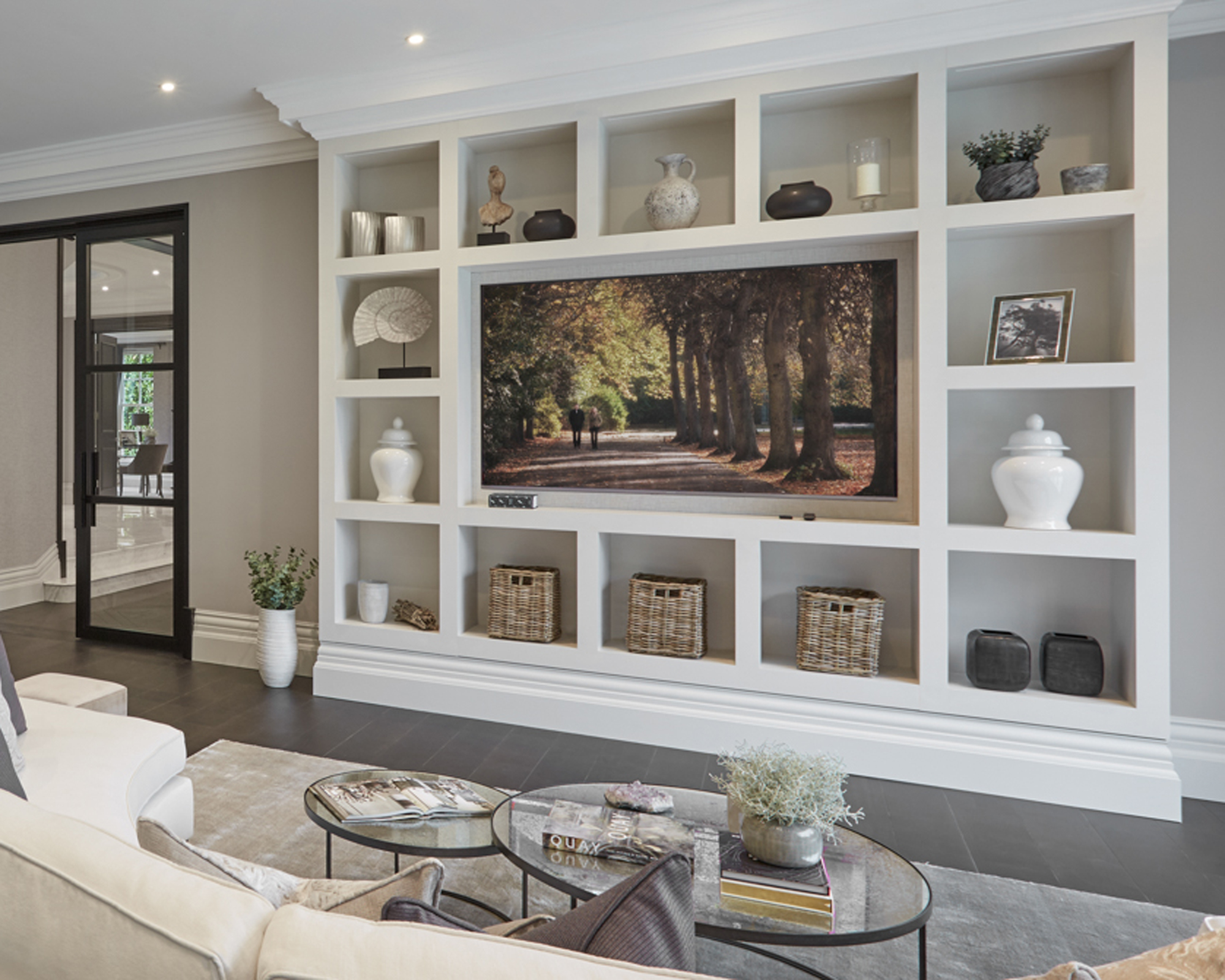 White wooden shelving unit displaying a TV recessed into a wall, with a neutral living room scheme