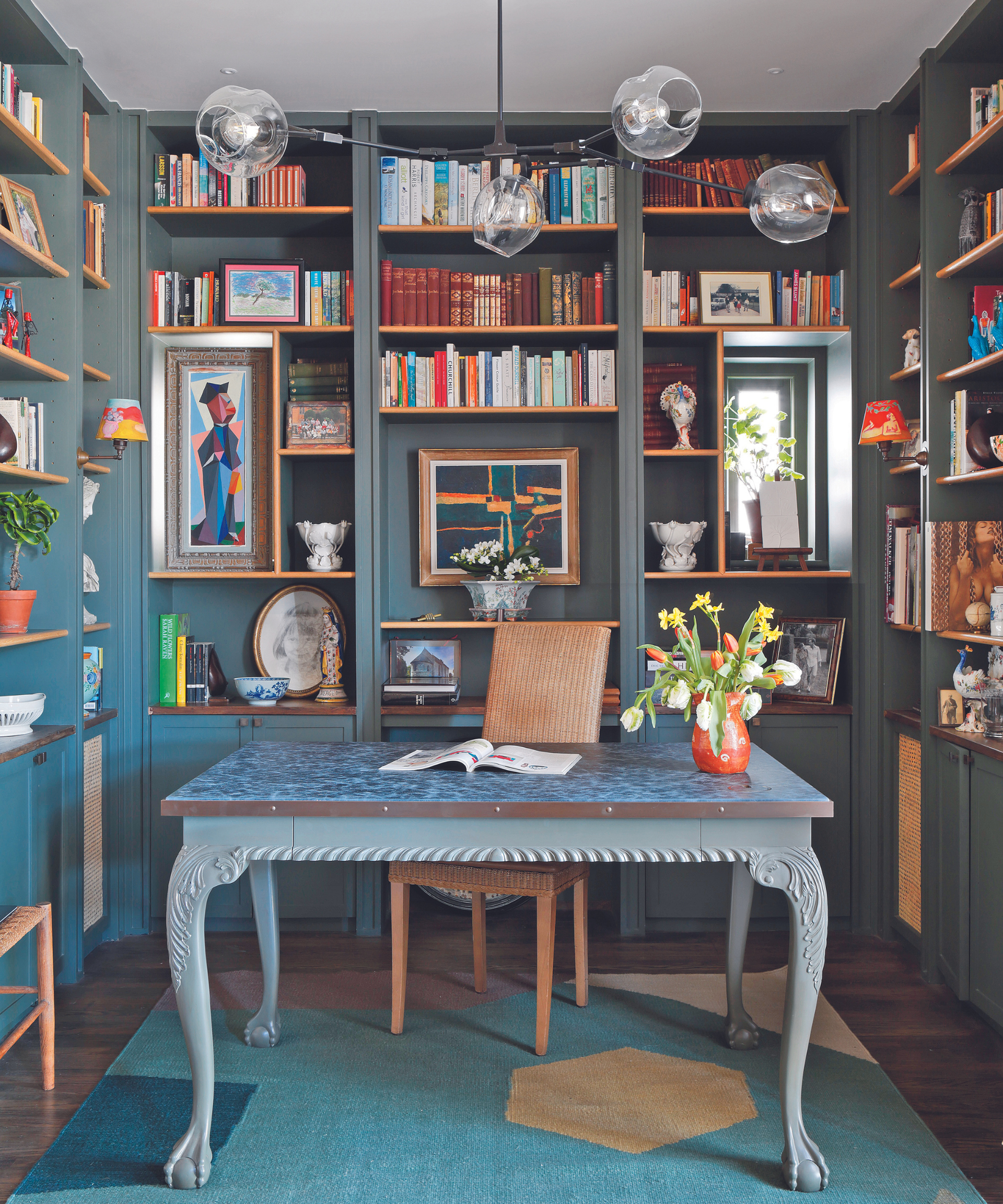 office desk in office room with bookshelf lined walls and pendant light with blue rug and blue desk and teal bookshelves