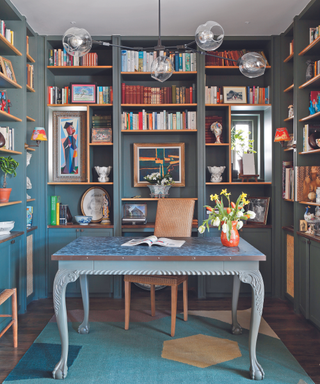 office desk in office room with bookshelf lined walls and pendant light with blue rug and blue desk and teal bookshelves