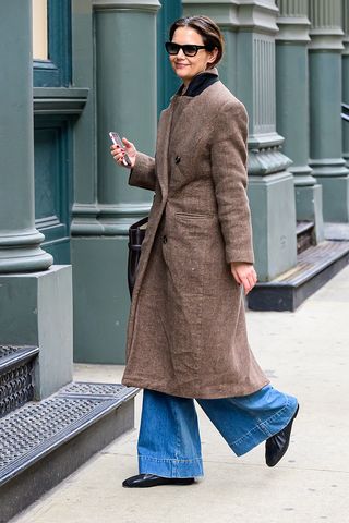 Katie Holmes wearing a brown coat, wide-leg jeans, and black ruched ballet flats in NYC.