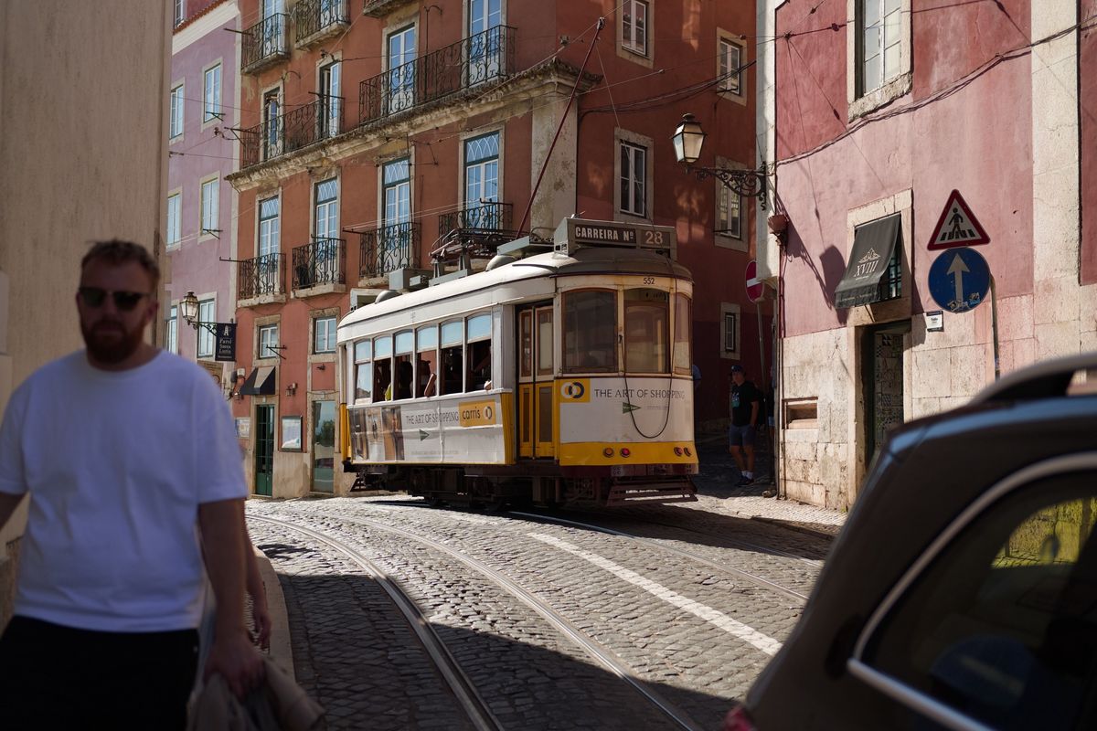 Traditional yellow Lisbon tram traveling along a narrow cobbled street between colorful historic buildings.