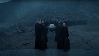 A group of sisters of the Bene Gesserit in Dune: Prophecy. There are two single-file lines of women dressed in long black robes. They are standing on a bleak, rocky landscape.
