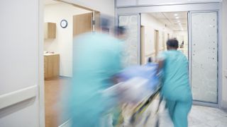 photo of three medical providers in blue scrubs rusing a person on a bed down a hospital hallway