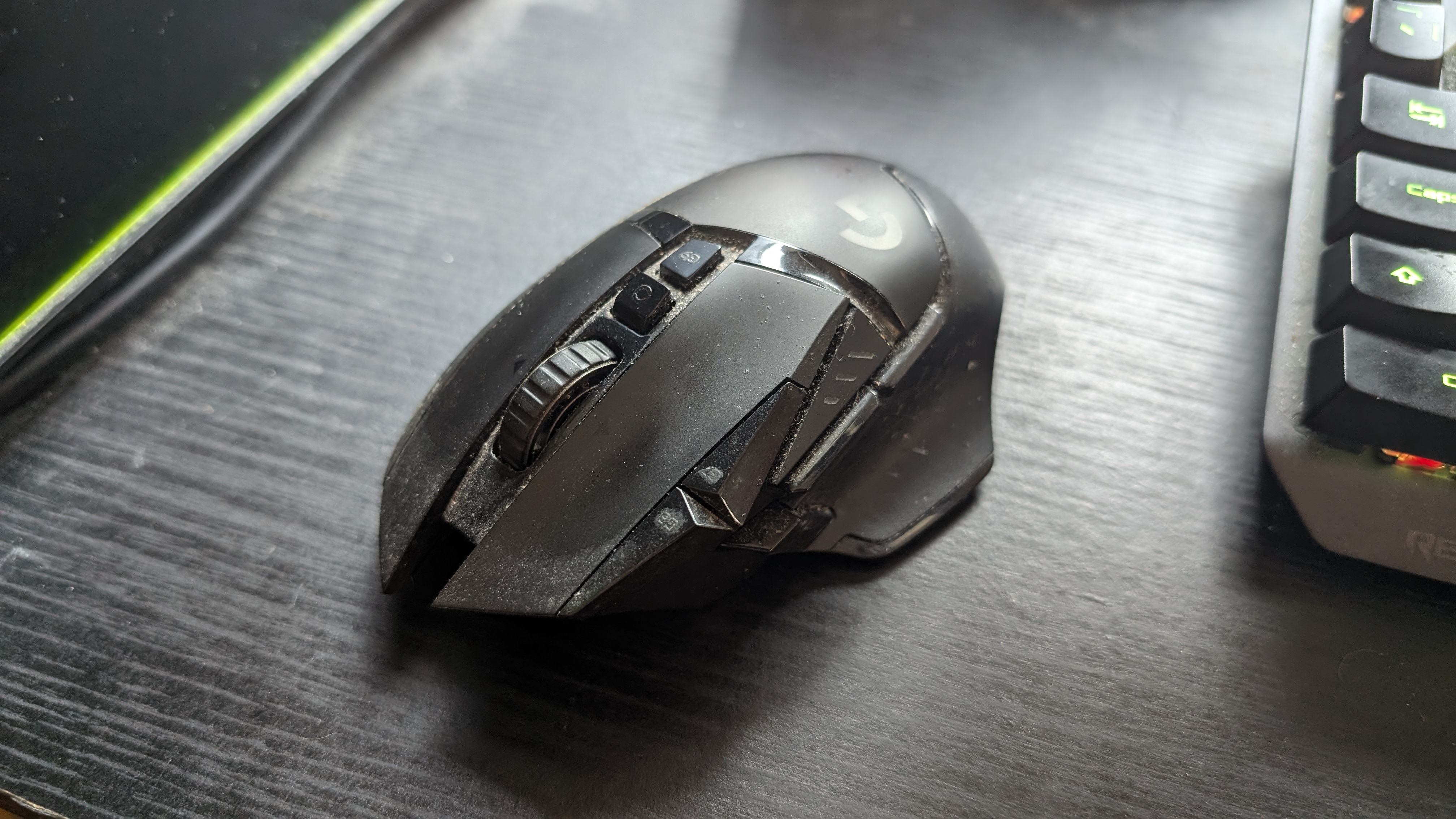 A heavily-used Logitech G502 Lightspeed Wireless gaming mouse sitting on a desk.