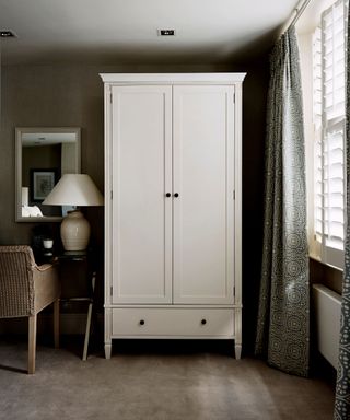 Large white wardrobe on a grey carpet next to a window with venetian blinds.
