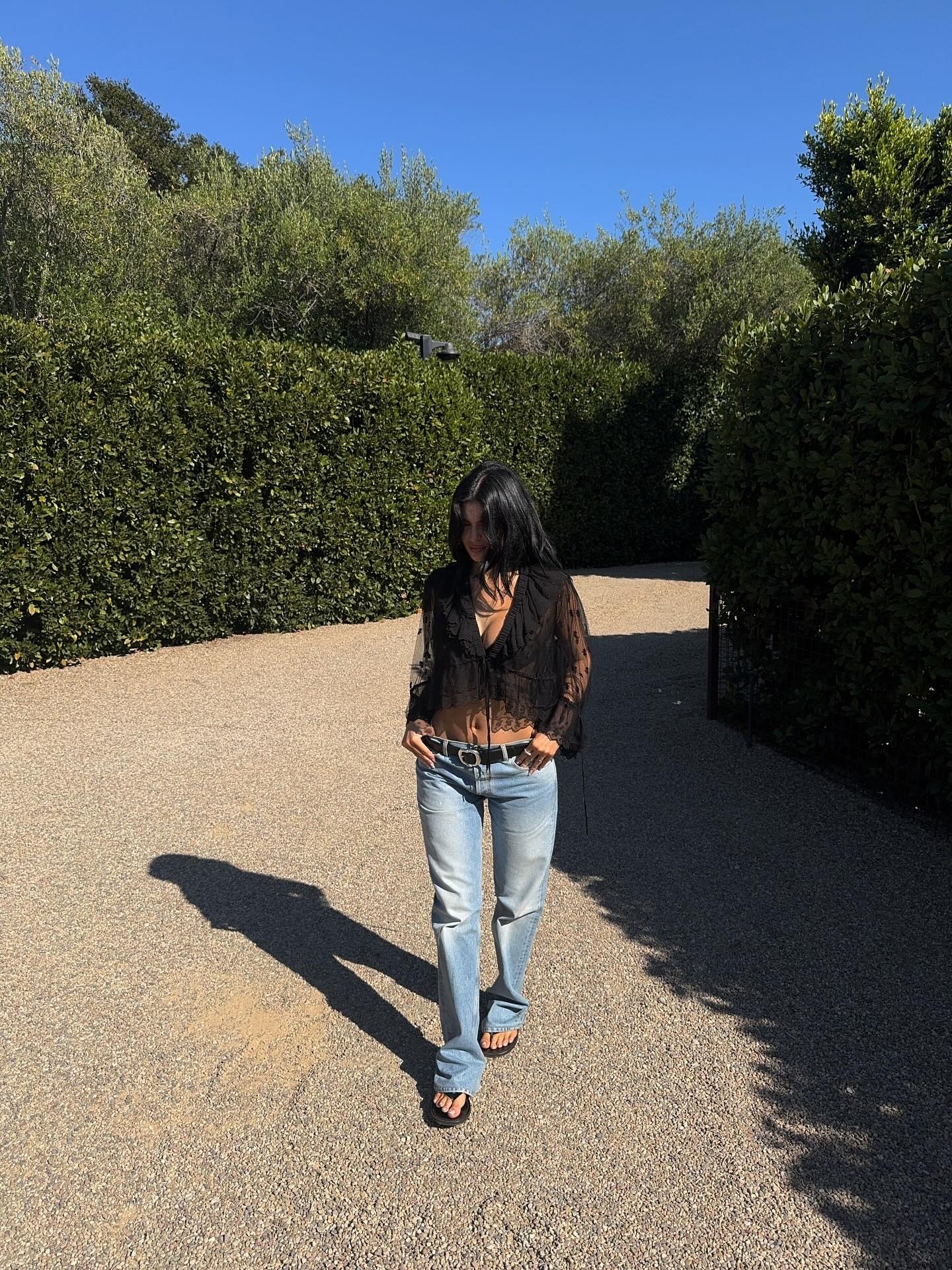 Kylie wears a black lace blouse, black belt, low-rise jeans, and black flip-flops.