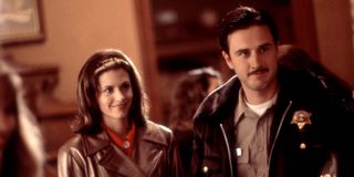 Gale Weathers (Courtney Cox) and Dewey Riley (David Arquette) stand together and smile in 'Scream'