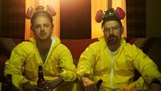 Actors Bryan Cranston and Aaron Paul, wearing yellow hazmat suits, sipping beer on sofa in a scene from Breaking Bad, the hit AMC crime series&nbsp;&ndash; here's where to watch and stream seasons 1-5